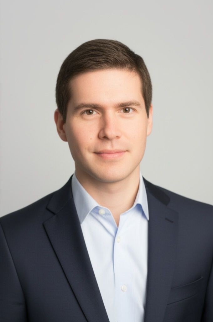 Person in a formal navy blue suit with a light blue dress shirt standing against a plain background.